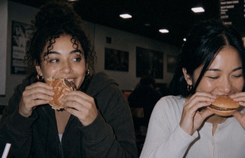 Two friends laughing while eating burgers