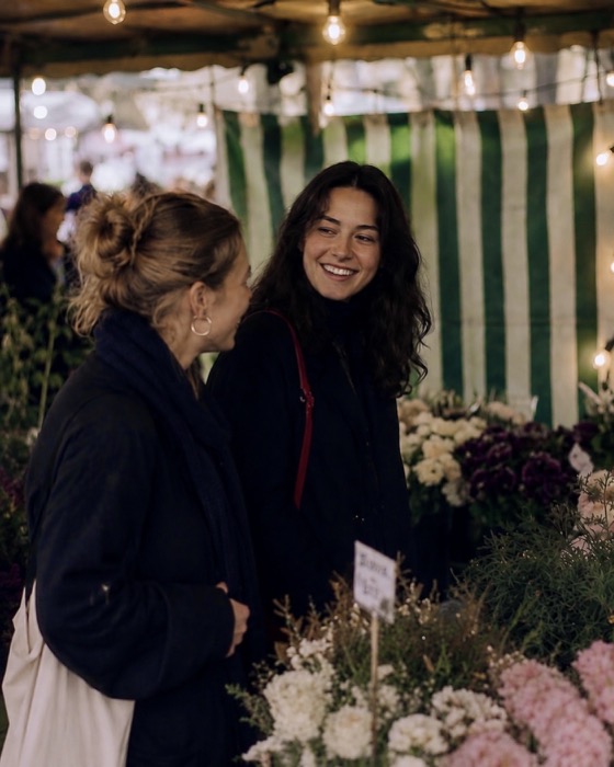 Two friends chatting among flowers at an outdoor market